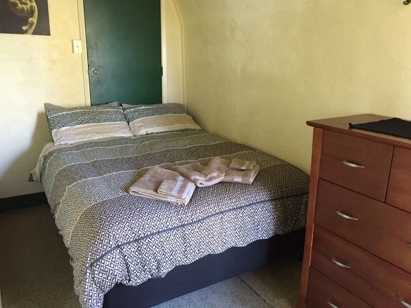A bedroom with a bed, pillows, a wooden dresser, and a green door.