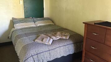A bedroom with a bed, pillows, a wooden dresser, and a green door.