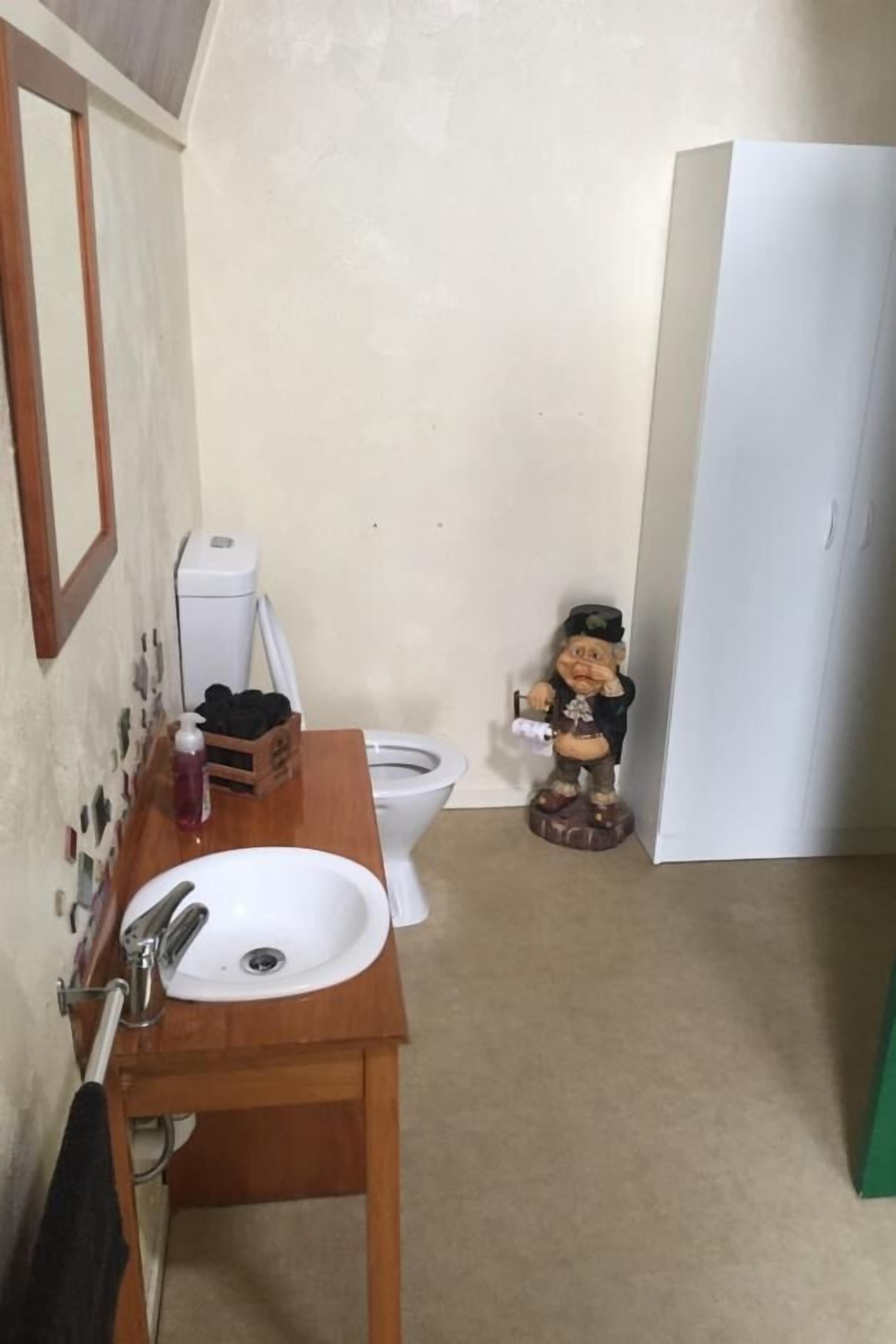 A small bathroom with a wooden vanity, a white sink, a toilet, and a decorative figure.