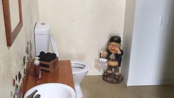 A small bathroom with a wooden vanity, a white sink, a toilet, and a decorative figure.