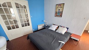 A bedroom with a bed, a desk, a chair, a radiator, and a door.