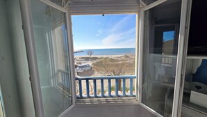A room with a large open window, a view of the beach, and a blue railing.