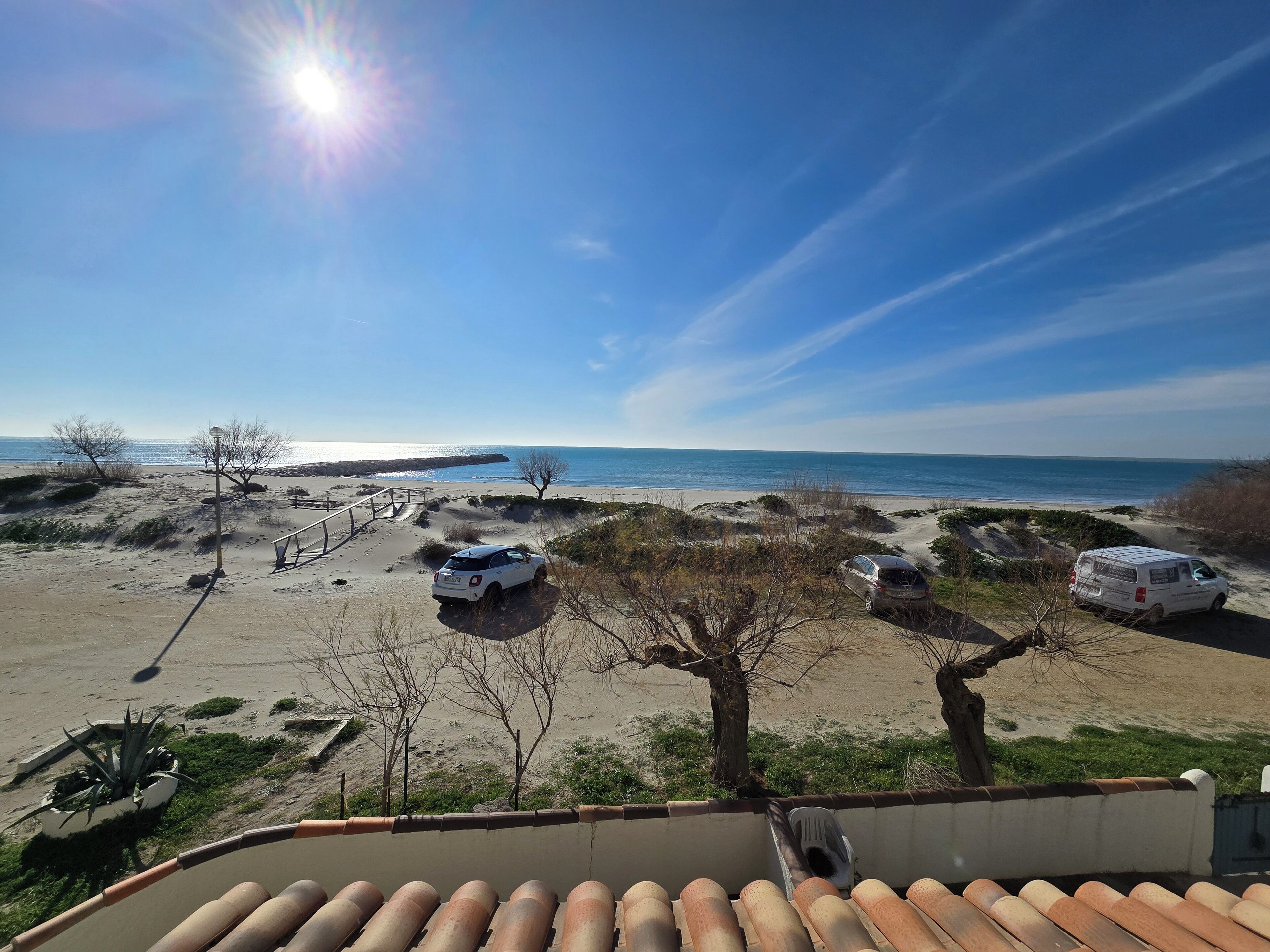 Blick auf einen Strand mit geparkten Fahrzeugen und blauem Himmel.
