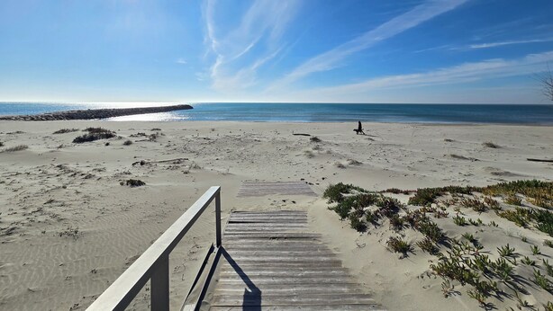 A beach with a wooden boardwalk leading to the water, clear skies, and a calm sea.