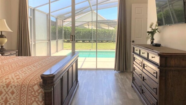 A bedroom with a large bed, a dresser, and a sliding glass door leading to a pool area. - Mickeys Paradise Glenbrook Resort -5* Bed, 3 &1/2 Bath Villa with Pool and Spa. (Clermont)