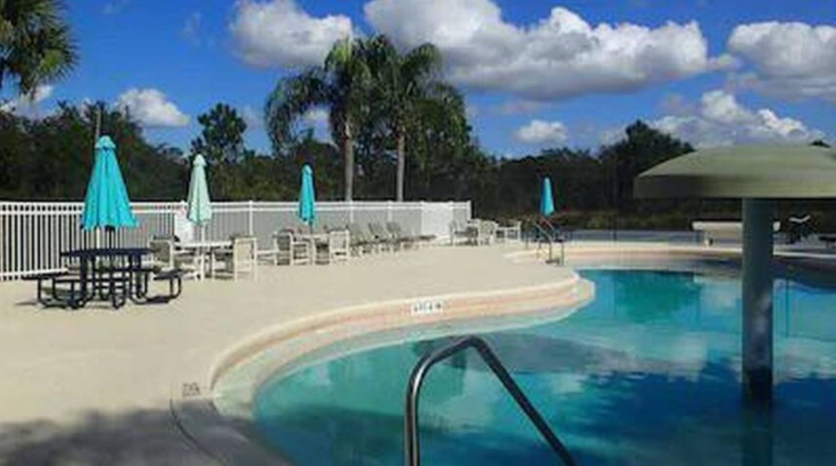 A pool area with lounge chairs and umbrellas, surrounded by palm trees and a clear sky.