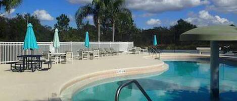 A pool area with lounge chairs and umbrellas, surrounded by palm trees and a clear sky.