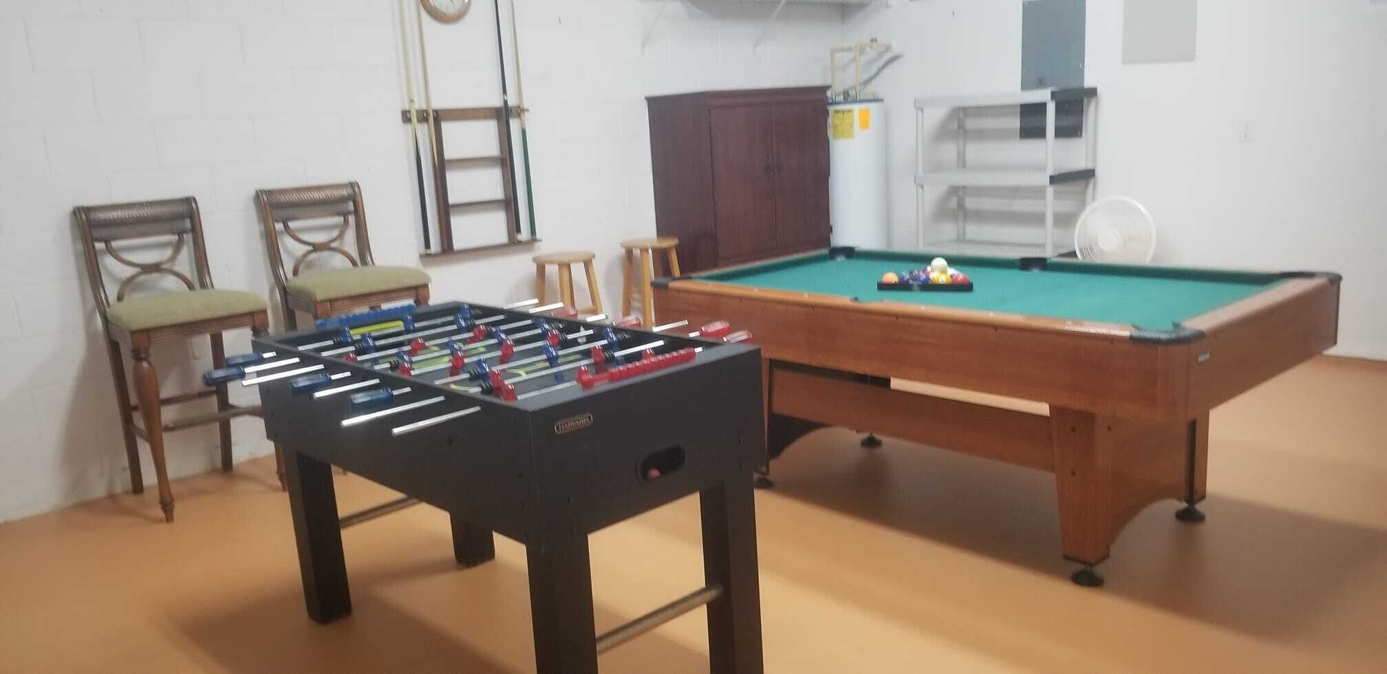 Una habitación con mesa de futbolín, mesa de billar y dos sillas.