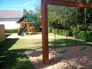 Playful backyard oasis with a swing set and slide, surrounded by lush greenery.