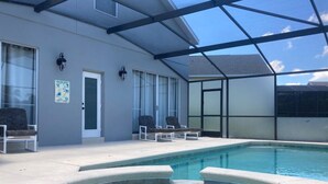 A pool area with a glass-enclosed structure, lounge chairs, and a door with a poster. - Mickeys Paradise Glenbrook Resort -5* Bed, 3 &1/2 Bath Villa with Pool and Spa. (Clermont)