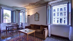 Ein Zimmer mit einer braunen Couch, einem Holztisch und einem gemusterten Teppich. Ein großes Fenster bietet Blick auf ein Gebäude.