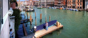 A canal with boats docked, a wooden pier, and buildings in the background.
