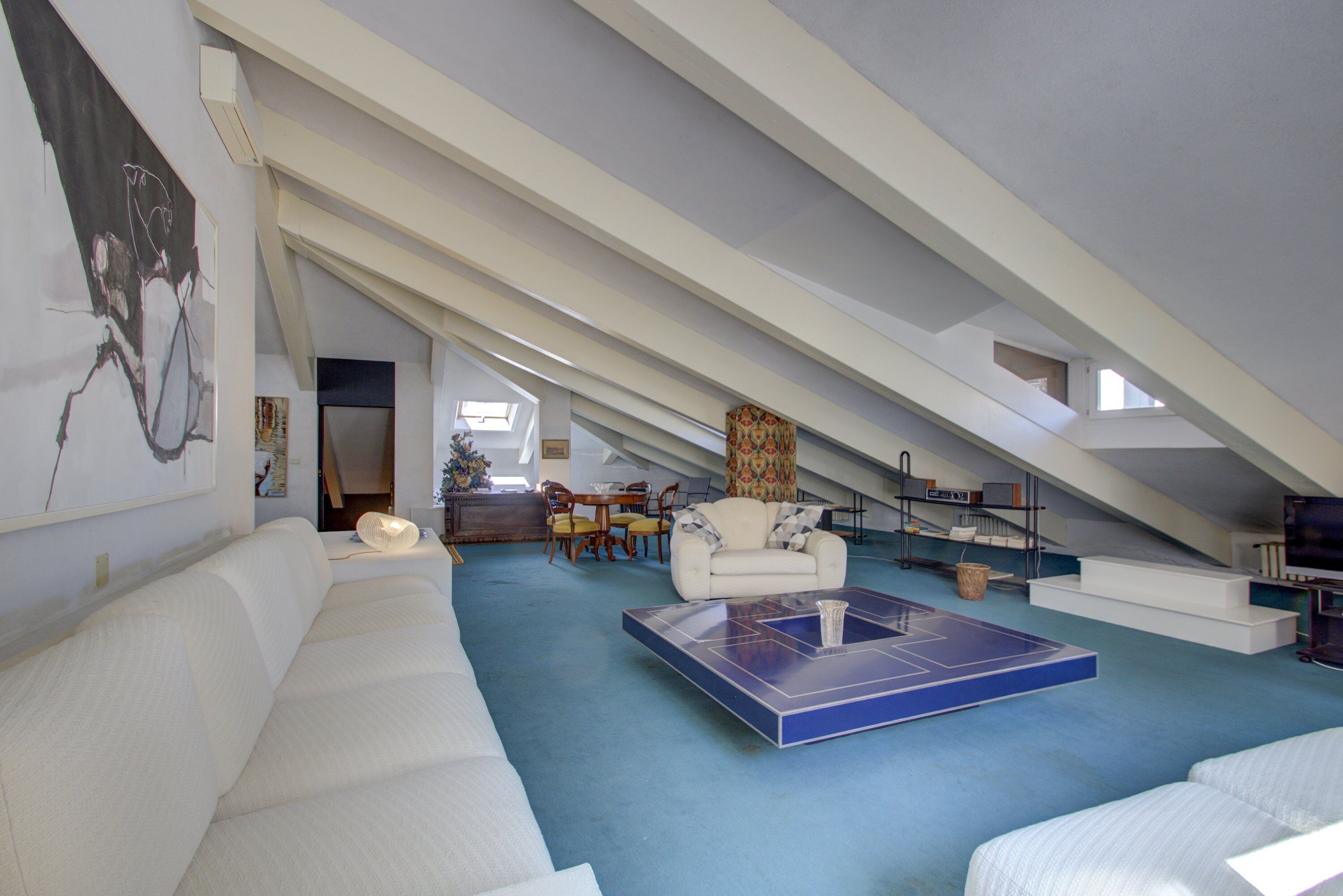Un loft spacieux avec un plafond haut, un grand canapé blanc, une table de ping-pong et un coin repas avec des chaises et une table.