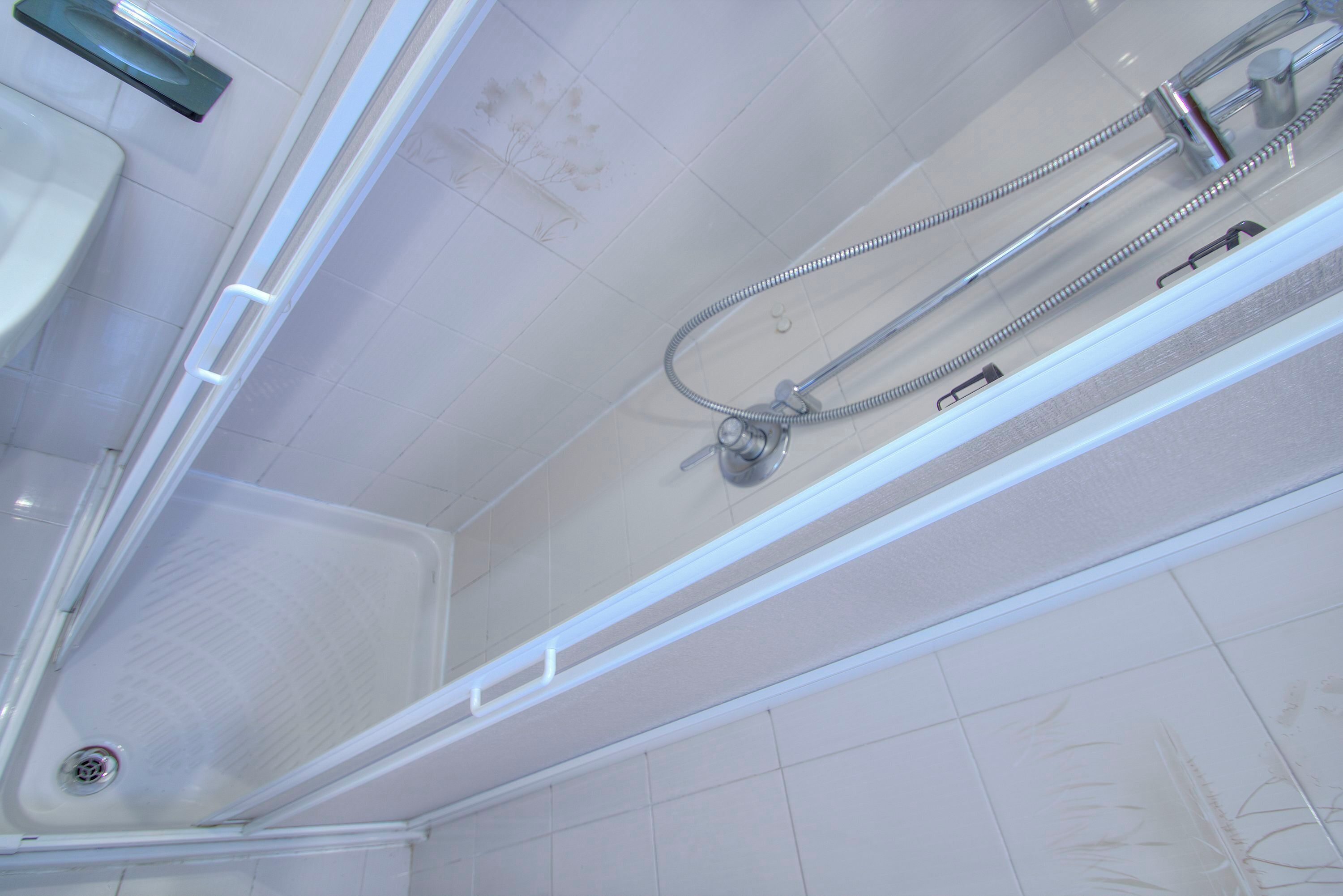 A modern bathroom with a glass-enclosed shower, a visible drain, and a tiled floor.