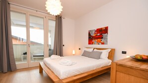 A modern bedroom with a wooden bed, a glass door leading to a balcony, and a red abstract painting on the wall. - Aurora Home (Sirmione)