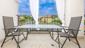 A balcony with a glass table and two chairs, a view of a residential area, and a white curtain. - Aurora Home (Sirmione)