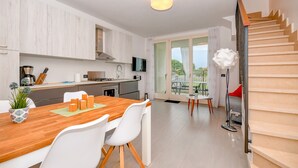 A modern kitchen with white cabinetry, a wooden dining table, and a staircase leading to a balcony. - Aurora Home (Sirmione)