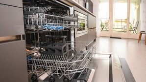 An open dishwasher with racks and utensils inside. - Aurora Home (Sirmione)