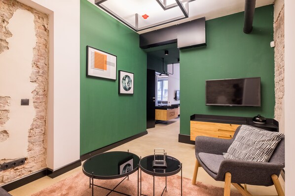 Una sala de estar moderna con paredes verdes, un muro de acento de piedra, un televisor de pantalla plana, un sofá gris con un cojín estampado y una pequeña mesa de centro.