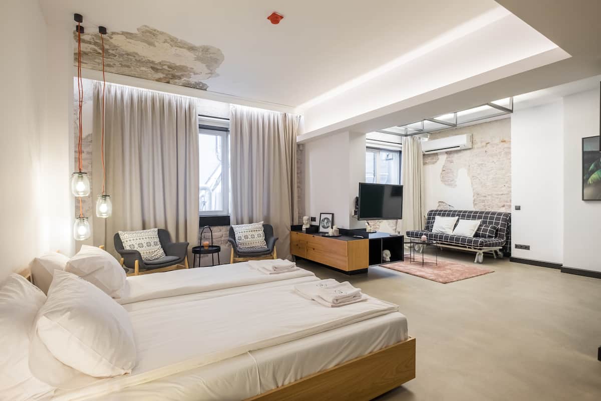 Habitació d'hotel moderna amb un llit gran, dos seients, un sofà, un televisor i un armari de fusta.