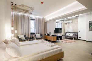 Una habitación de hotel moderna con una cama grande, dos sillones, un sofá, un televisor y un mueble de madera.