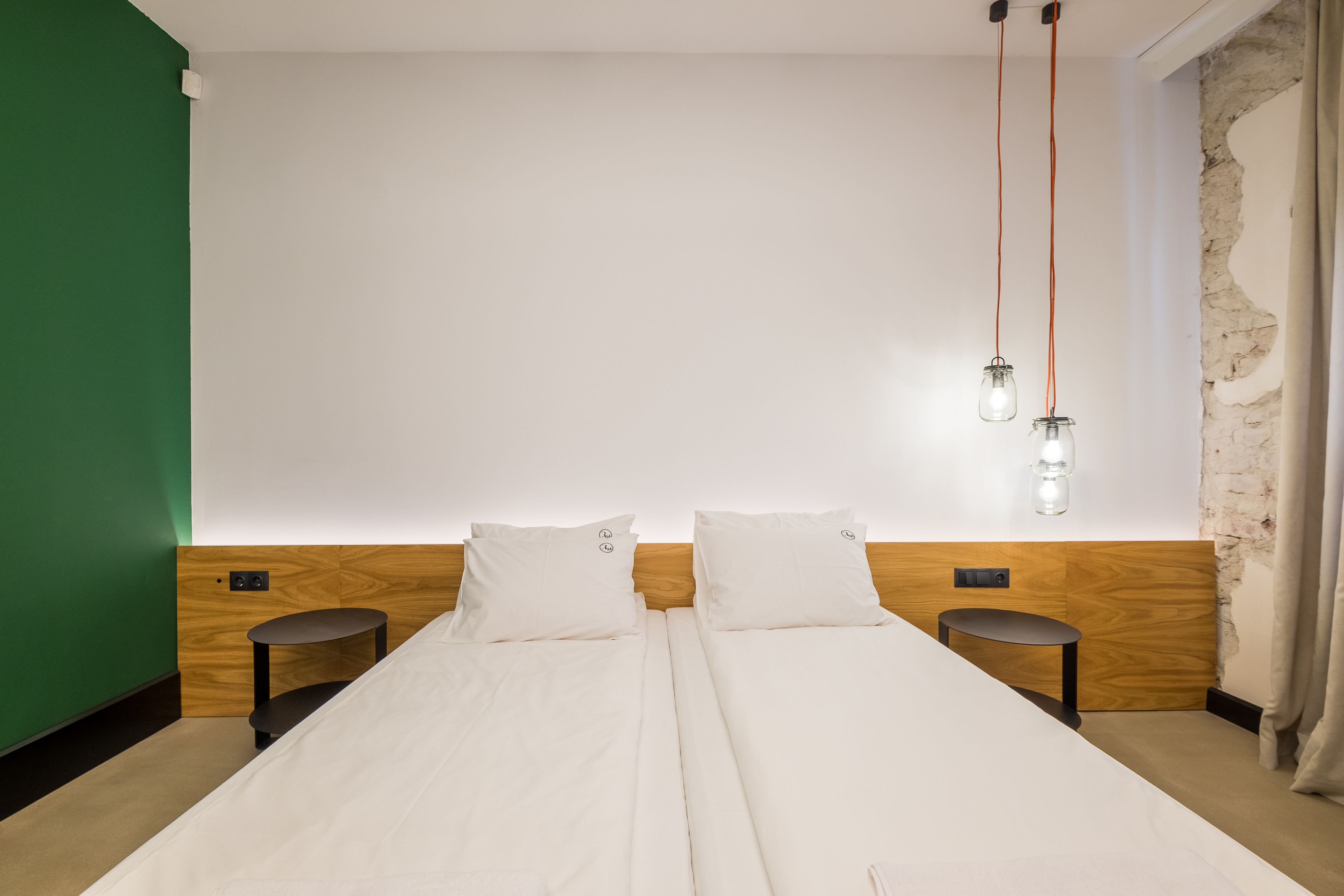 Un lit double avec une literie blanche, deux tables de chevet, une tête de lit en bois et un luminaire fixé au mur.