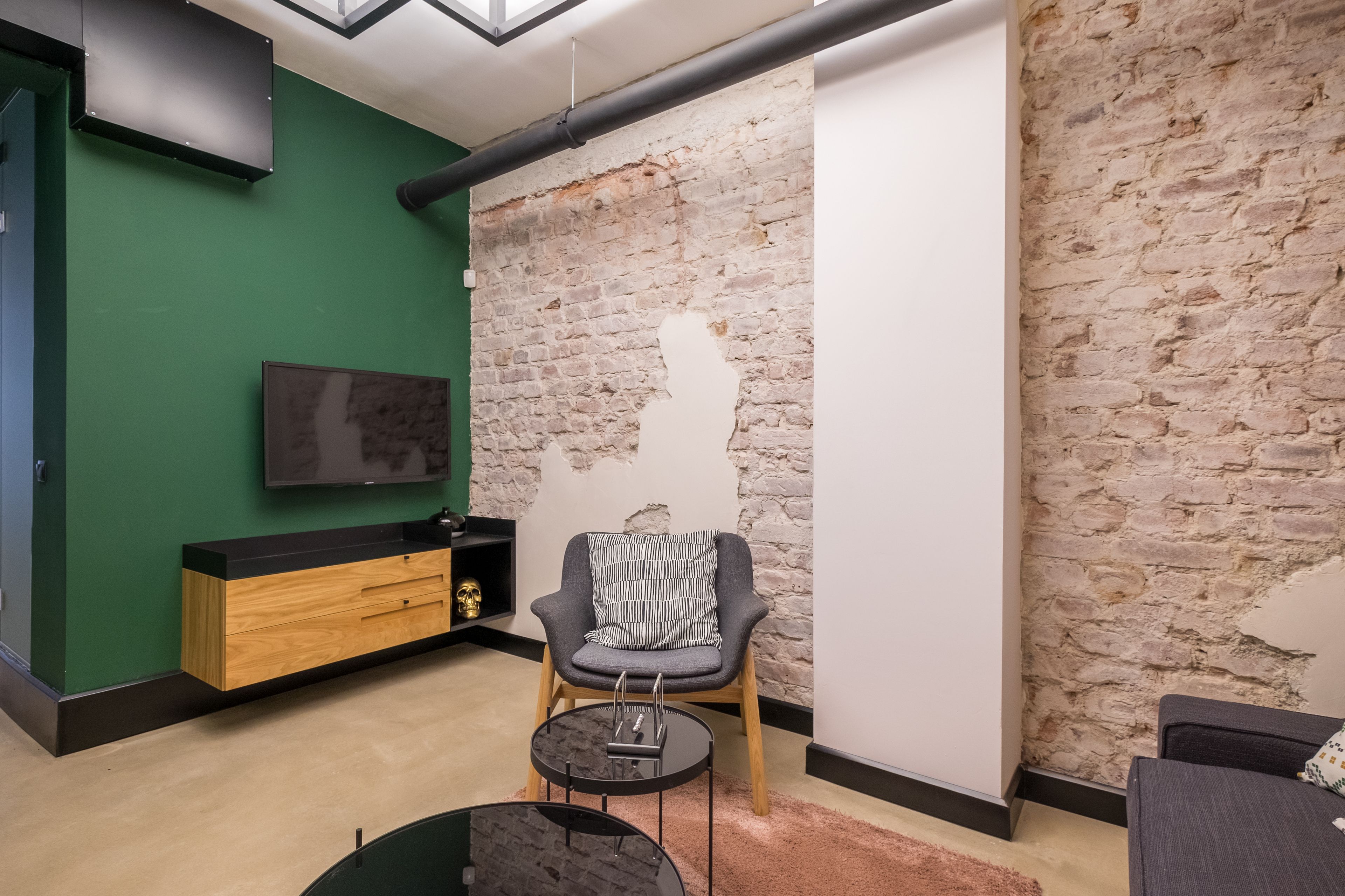 Een moderne woonkamer met een groene wand, een bakstenen wand en een houten kast.
