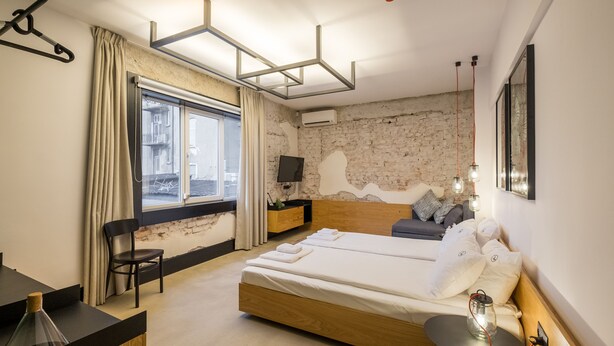 A modern bedroom with a large bed, a desk, a chair, a TV, and a window with curtains. - R34 Boutique Hotel (Sofia)
