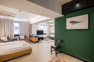 A modern hotel room with a bed, seating area, TV, and artwork on the wall.