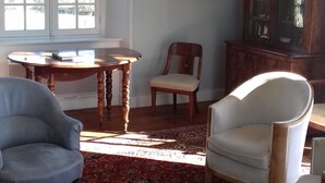 A room with a chandelier, a painting, a wooden cabinet, and a patterned rug.