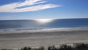 Een strand met een heldere lucht en de zon die op het water glinstert.