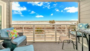 Een balkon met uitzicht op het strand, rieten meubels en een houten hek.