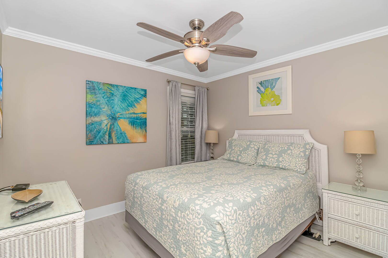 A bedroom with a bed, a ceiling fan, a nightstand, a lamp, and artwork on the walls.