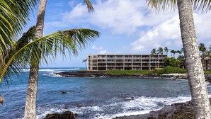 Hotel frente al mar con diseño moderno, cerca del océano, con olas visibles y palmeras.