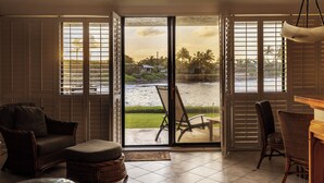 Habitación con vista a un cuerpo de agua, una silla, una mesa y un reposapiés de mimbre.