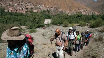 Un grupo de excursionistas en un sendero rocoso con un pueblo al fondo.
