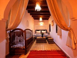 Um quarto com cama de madeira, mesa de cabeceira, tapete vermelho e um lustre.