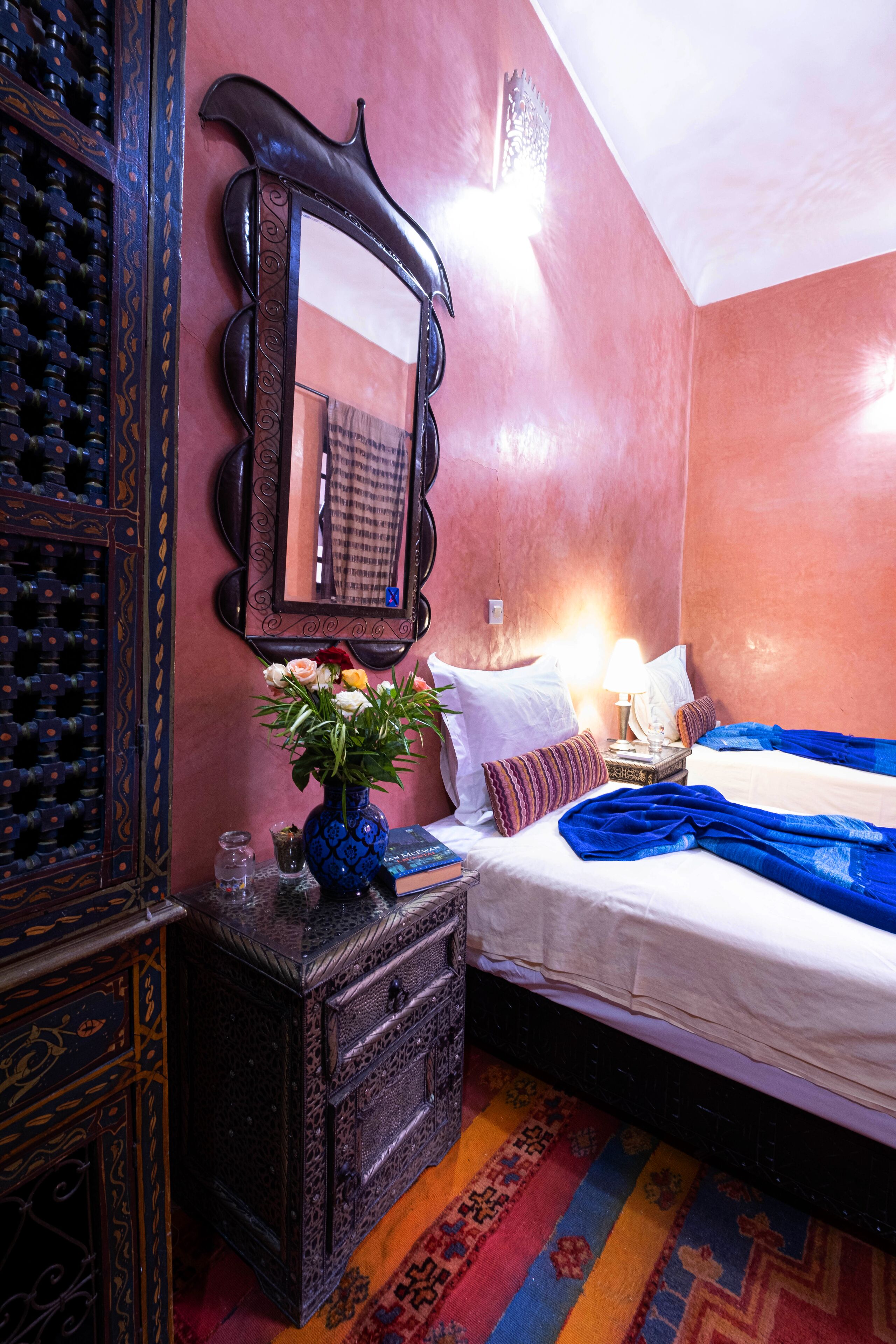 Un dormitorio con cama, cómoda, espejo y un florero con flores.