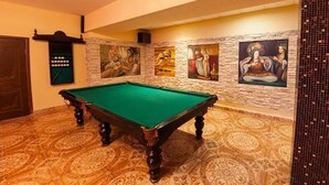 Una mesa de billar en una habitación con alfombra estampada y una pared decorada con pinturas.