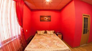 Un dormitorio con una pared roja, una cama con colcha estampada, una mesita de noche y una puerta.