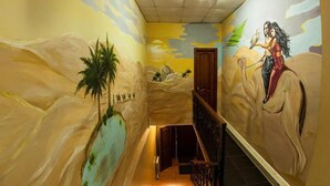 Un pasillo con un mural de una escena desértica, una escalera de madera y una puerta al final.