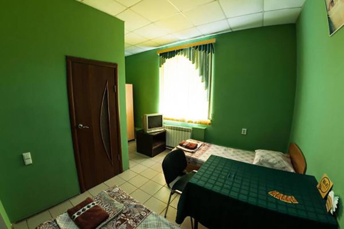 Una habitación pequeña con paredes verdes, dos camas individuales, un escritorio, una silla, un televisor y una puerta.