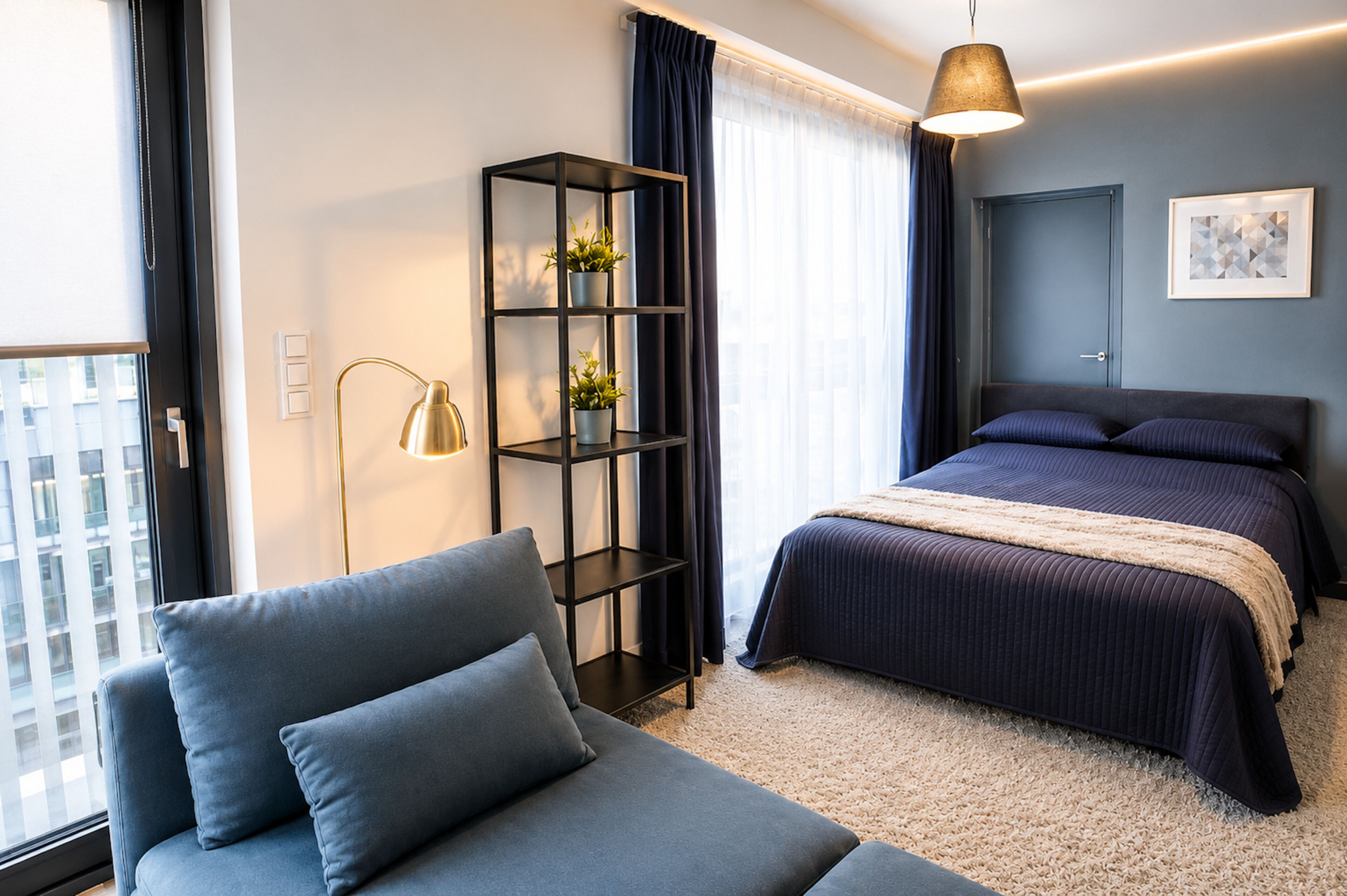 A modern hotel room with a bed, a seating area, a bookshelf, and a window with curtains.