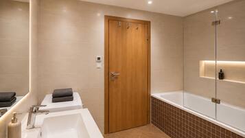 A modern bathroom with a wooden door, a white sink, a bathtub, and a mirror.
