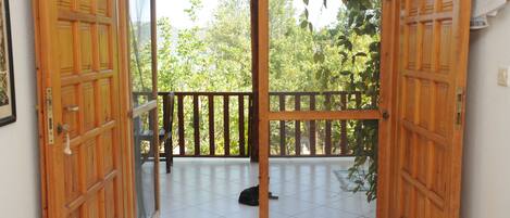 An open wooden door leading to a balcony with a tiled floor and a black cat lying on it.