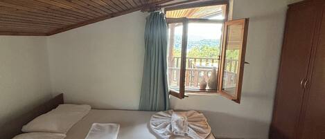 A bedroom with a wooden ceiling, a bed with neatly folded towels, a window with a view, and a wardrobe.