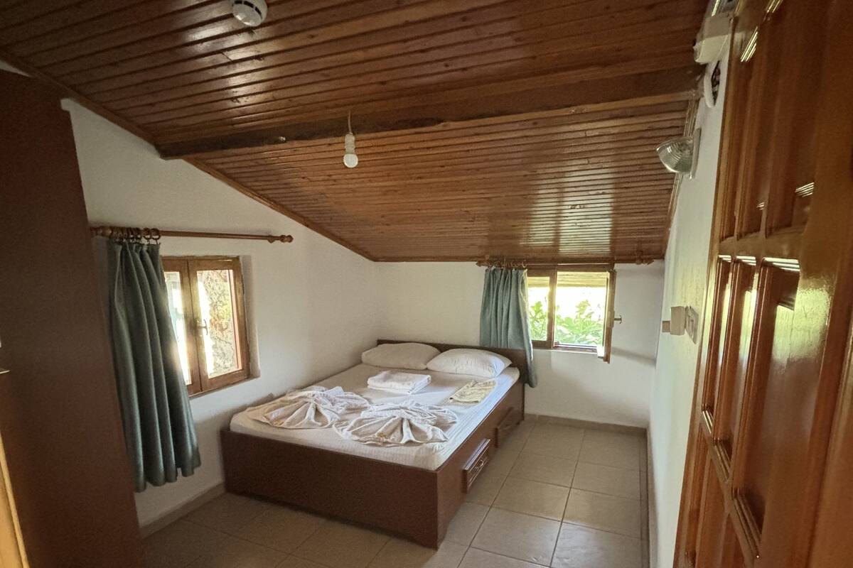A bedroom with a wooden ceiling, a bed, a window with curtains, and a wooden wardrobe.