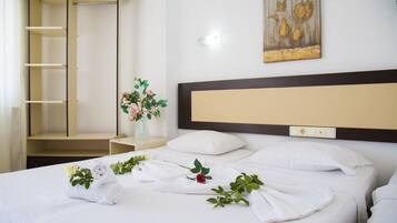 Ein Hotelzimmer mit einem ordentlich bezogenen Bett, einem Nachttisch mit Blumenvase, einem an der Wand hängenden Kunstwerk und einem Einbauschrank.