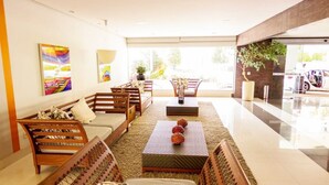 A modern hotel lobby with a seating area featuring sofas and a coffee table, a large window with a view of the outside, and a reception desk. - Veredas Rio Quente (Rio Quente)