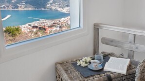 A room with a view of a coastal town, a wicker table with a book, a cup, and a glass of water. - Villa Savvina (Skopelos)